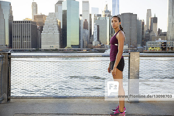 Portrait of female athlete standing on promenade by river
