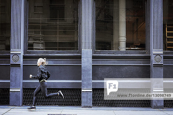 Seitenansicht einer Athletin  die auf einem Fußweg durch ein Gebäude in der Stadt läuft