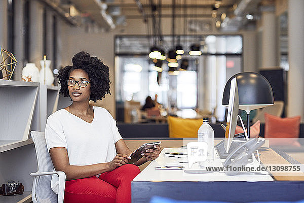 Geschäftsfrau schaut weg  während sie einen Tablet-Computer im Büro hält