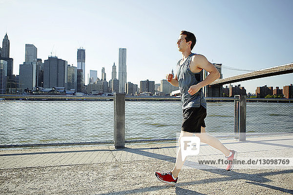 Side view of man jogging on pathway by East River against sky