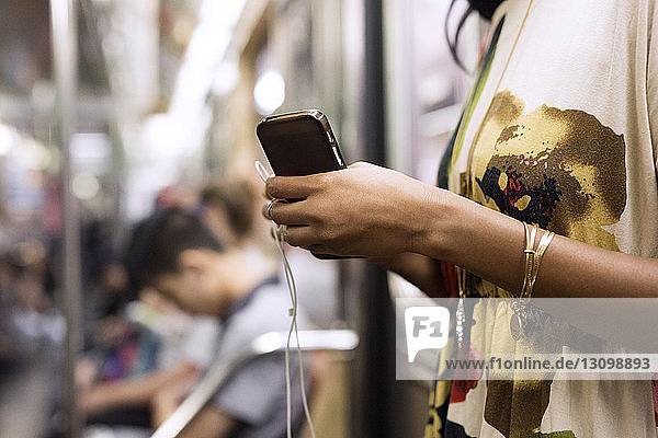 Mittelsektion einer Frau  die Mobiltelefon und Kopfhörer im Zug hält