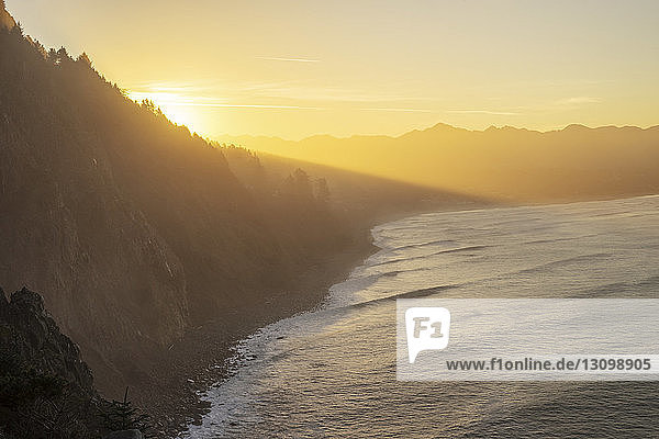 High angle view of silhouette cliff by sea against sky