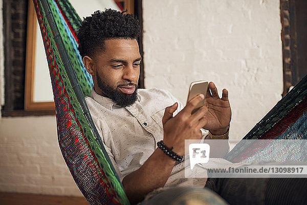 Man using smart phone while sitting on hammock at home
