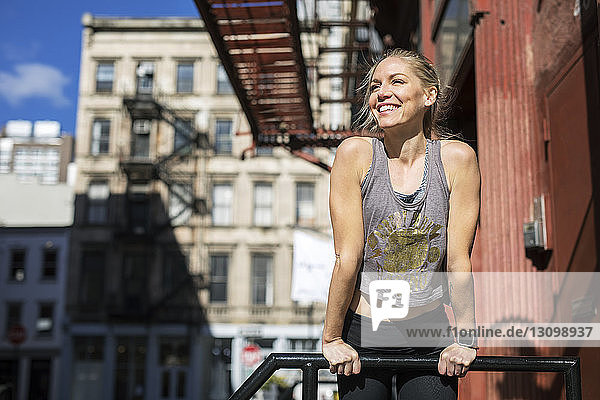 Smiling athlete looking away while standing by railing during sunny day