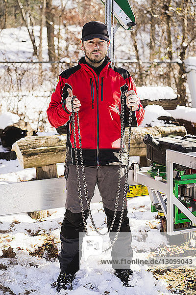 Portrait of worker holding chains while standing on snow covered field in backyard