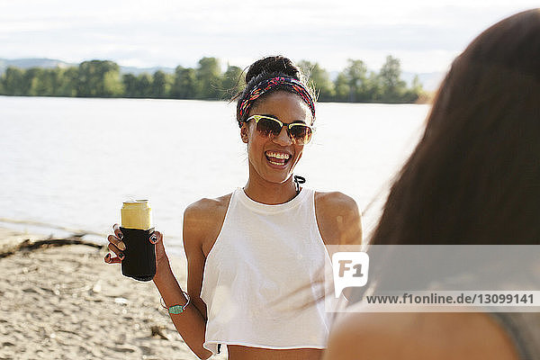 Happy woman holding can while looking at friend against river