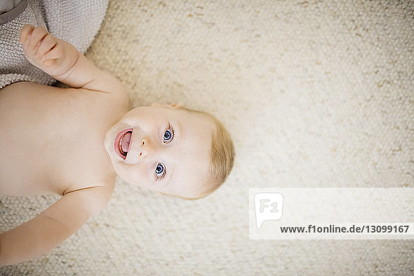 Draufsicht auf Baby  das lachend zu Hause auf dem Teppich liegt