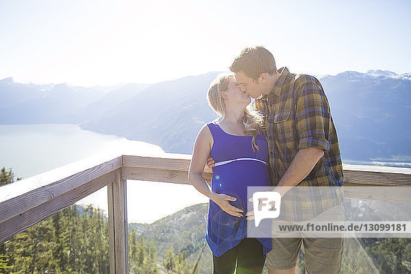 Paar küsst sich  während es am sonnigen Tag am Beobachtungspunkt vor den Bergen steht