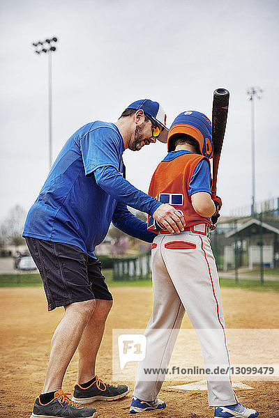 Side view of coach assisting boy in playing baseball on field