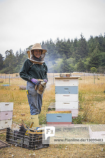 Porträt einer Bienenzüchterin in Arbeitsschutzkleidung  die bei den Bienenstöcken im Betrieb steht