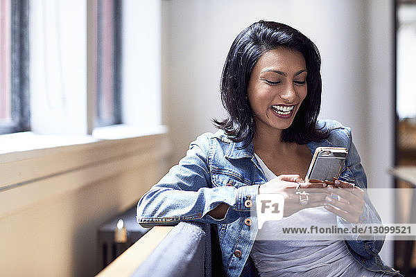 Fröhliche Geschäftsfrau benutzt ein Smartphone  während sie im Büro sitzt