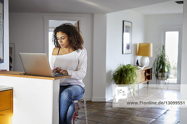 Frau benutzt Laptop-Computer  während sie zu Hause auf einem Stuhl sitzt