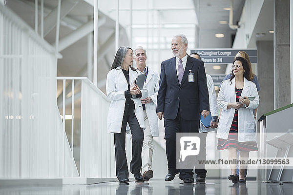 Senior doctor discussing with coworkers while walking in hospital corridor