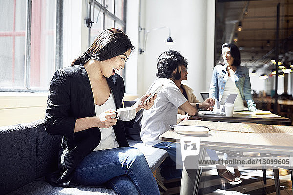 Happy businesswoman using smart phone with business people working in background