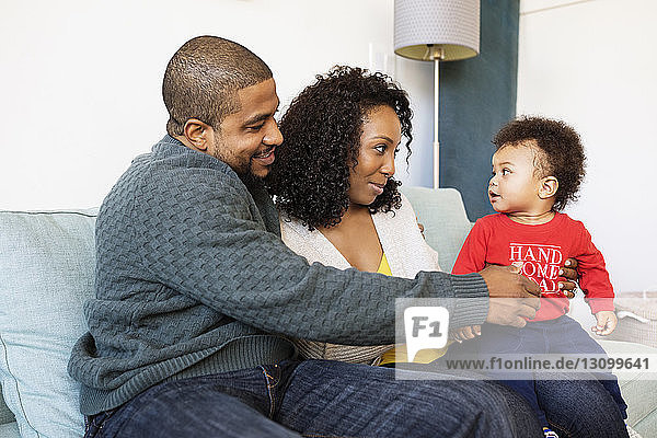 Loving parents looking at son while sitting on sofa