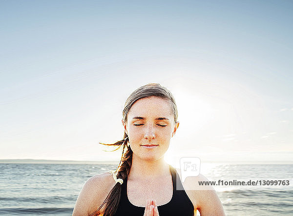 Woman meditating in lotus position by sea against sky