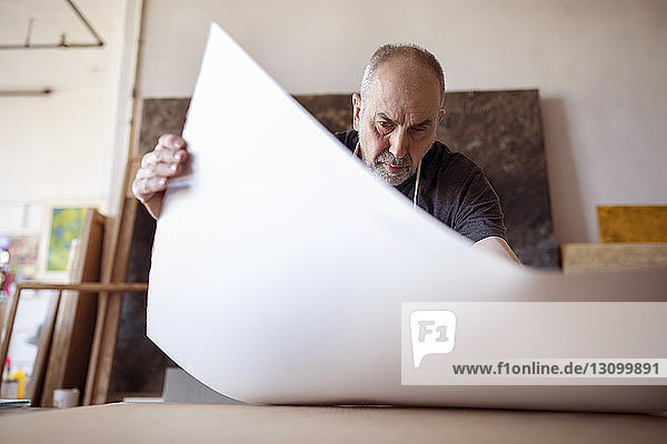 Low angle view of senior artist making painting at table in workshop