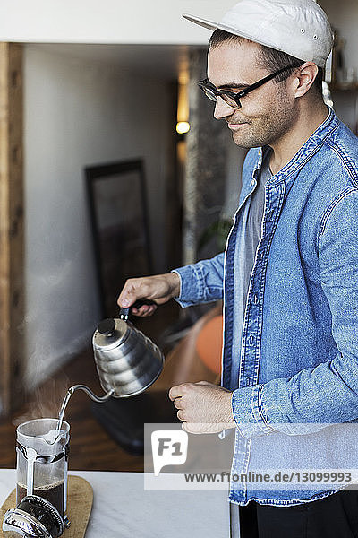 Mann gießt zu Hause kochendes Wasser in Kaffee