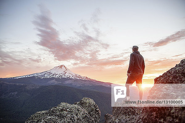 Rear view of hiker looking at view while standing on mountain during sunset