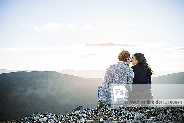 Rear view of couple sitting on rocks at mountain cliff