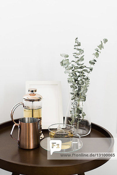 Getränke mit Bilderrahmen und Zimmerpflanze auf Tisch vor weißer Wand