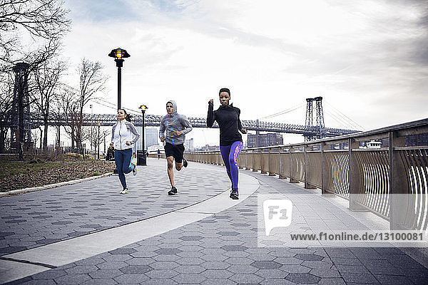 Engagierte multiethnische Athleten laufen auf einem Fußweg mit der Williamsburg-Brücke im Hintergrund