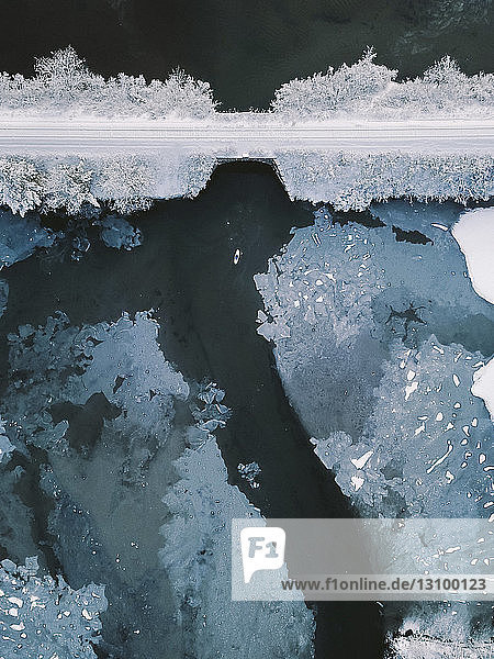 Hochwinkel-Distanzansicht einer Person  die im Winter auf einem See bei einer Brücke paddelt