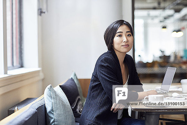 Porträt einer selbstbewussten Geschäftsfrau  die im Büro am Tisch sitzt