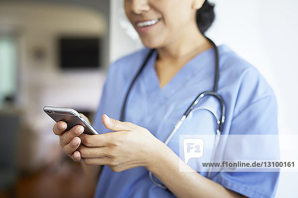Mittelsektion einer Ärztin  die während der Arbeit im Krankenhaus ein Smartphone benutzt