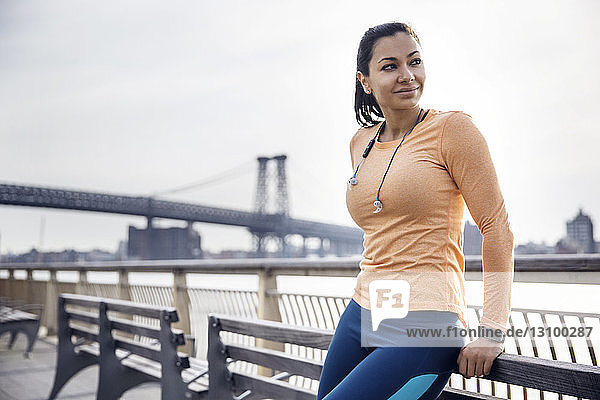Nachdenkliche Sportlerin lehnt auf Bank mit Williamsburg Bridge im Hintergrund
