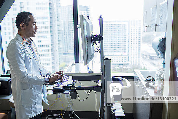 Männlicher Arzt benutzt Desktop-Computer  während er auf der Krankenhausstation steht