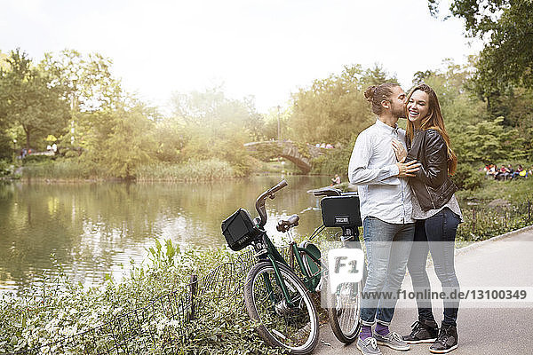 Man kissing girlfriend while standing with bicycles by lake