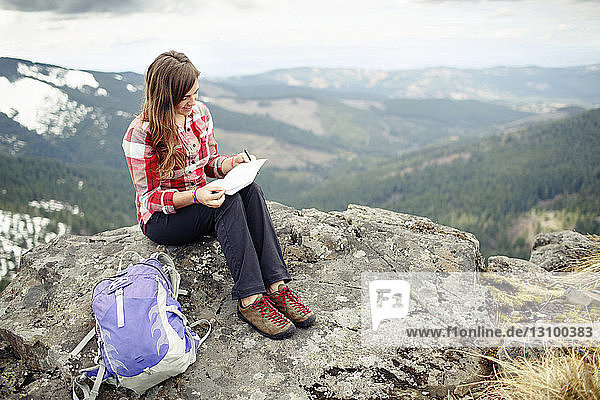 Smiling woman holding reading paper while sitting on mountain
