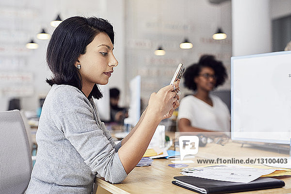Businesswoman using smart phone with female colleague sitting in background