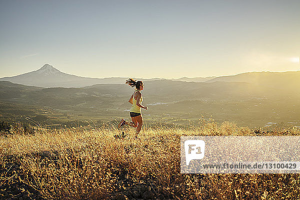 Frau in voller Länge joggt auf Berg vor klarem Himmel