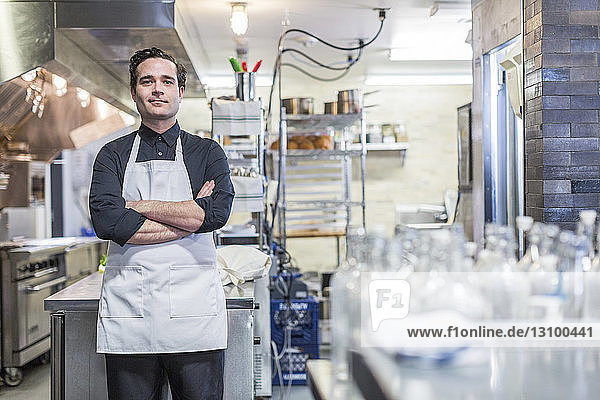Portrait of confident male chef with arms crossed standing at restaurant kitchen