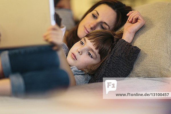 Mother and daughter using tablet computer while lying on sofa at home