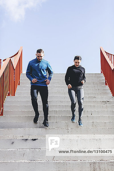 Low angle view of couple exercising on steps against sky