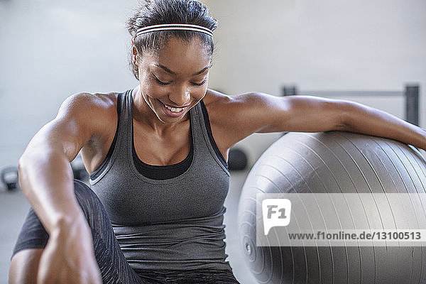 Lächelnder Athlet schaut beim Training mit Medizinball im Fitnessstudio nach unten