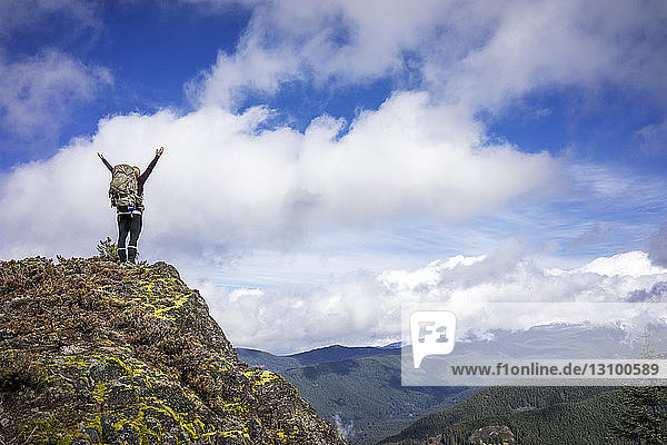 Low angle view of woman standing with arms raised on mountain against cloudy sky