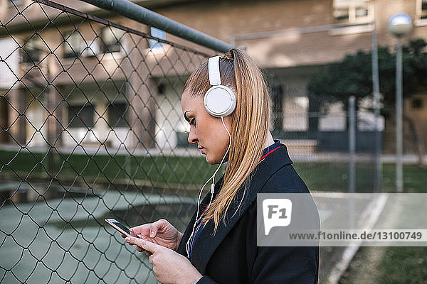 Side view of woman using mobile phone while standing by fence