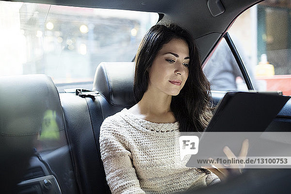 Young woman using tablet computer in taxi