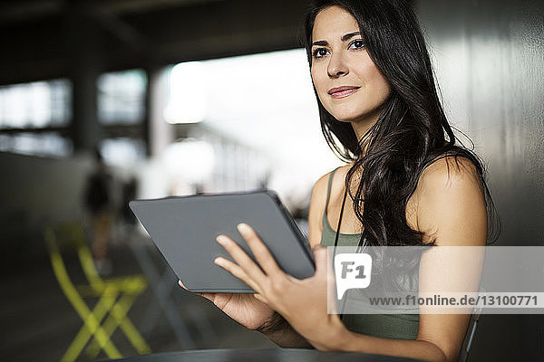 Nachdenkliche junge Frau hält Tablet-Computer im Freien