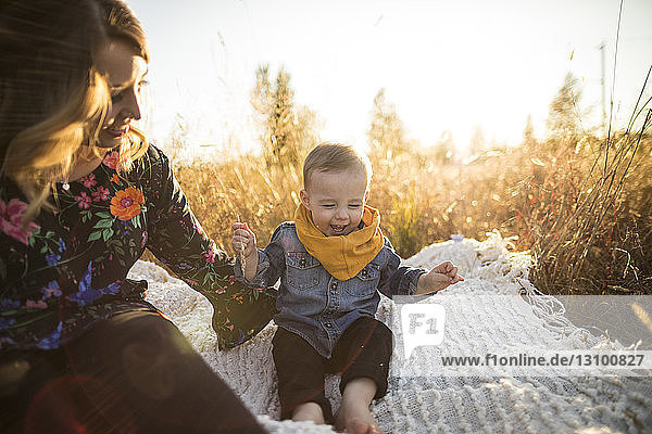 Mutter schaut auf glücklichen Sohn  der auf einer Picknickdecke auf dem Feld sitzt