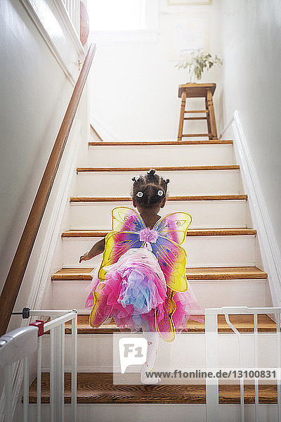 Rückansicht eines märchenhaft gekleideten Mädchens  das zu Hause die Treppe hinaufgeht