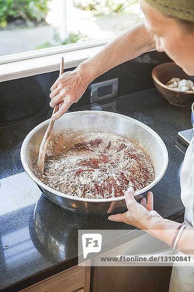 Ausgeschnittenes Bild einer Frau  die Zutaten in einem Behälter mischt  während sie an der Küchentheke steht