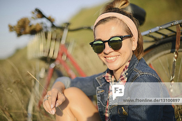 Portrait of cheerful woman wearing sunglasses against bicycle on field