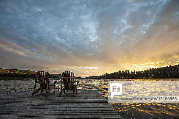 Chairs on pier by Lac Le Jeune lake at Paul Lake Provincial Park against sky during sunset