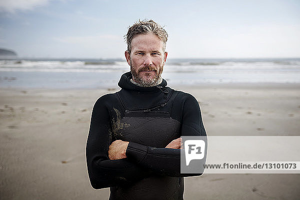 Porträt eines reifen Surfers  der mit verschränkten Armen am Strand steht