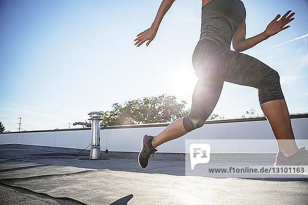 Low section of athlete running on building terrace against sky during sunny day